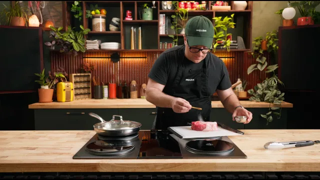A cook slicing meat beside a pan on an Impulse cooktop