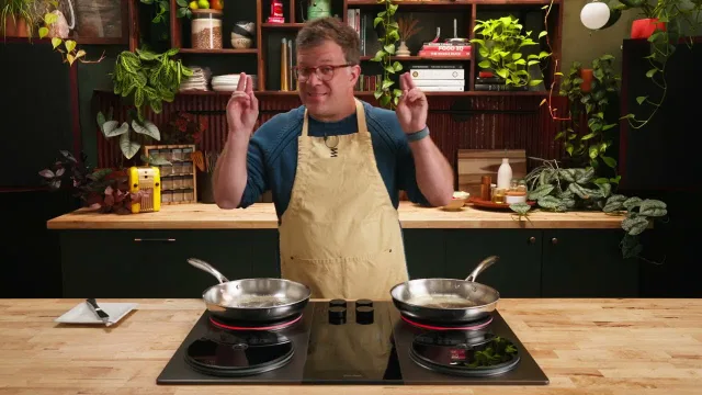 A cook in an apron beside two pans on an Impulse cooktop